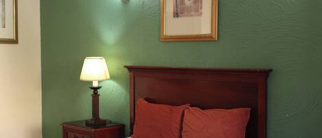 A neatly made bed with a wooden headboard, a bedside table with a lamp, and a framed picture on the wall.