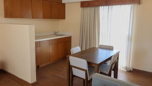 Een keuken met houten kastjes, een eettafel met stoelen en een raam met gordijnen.