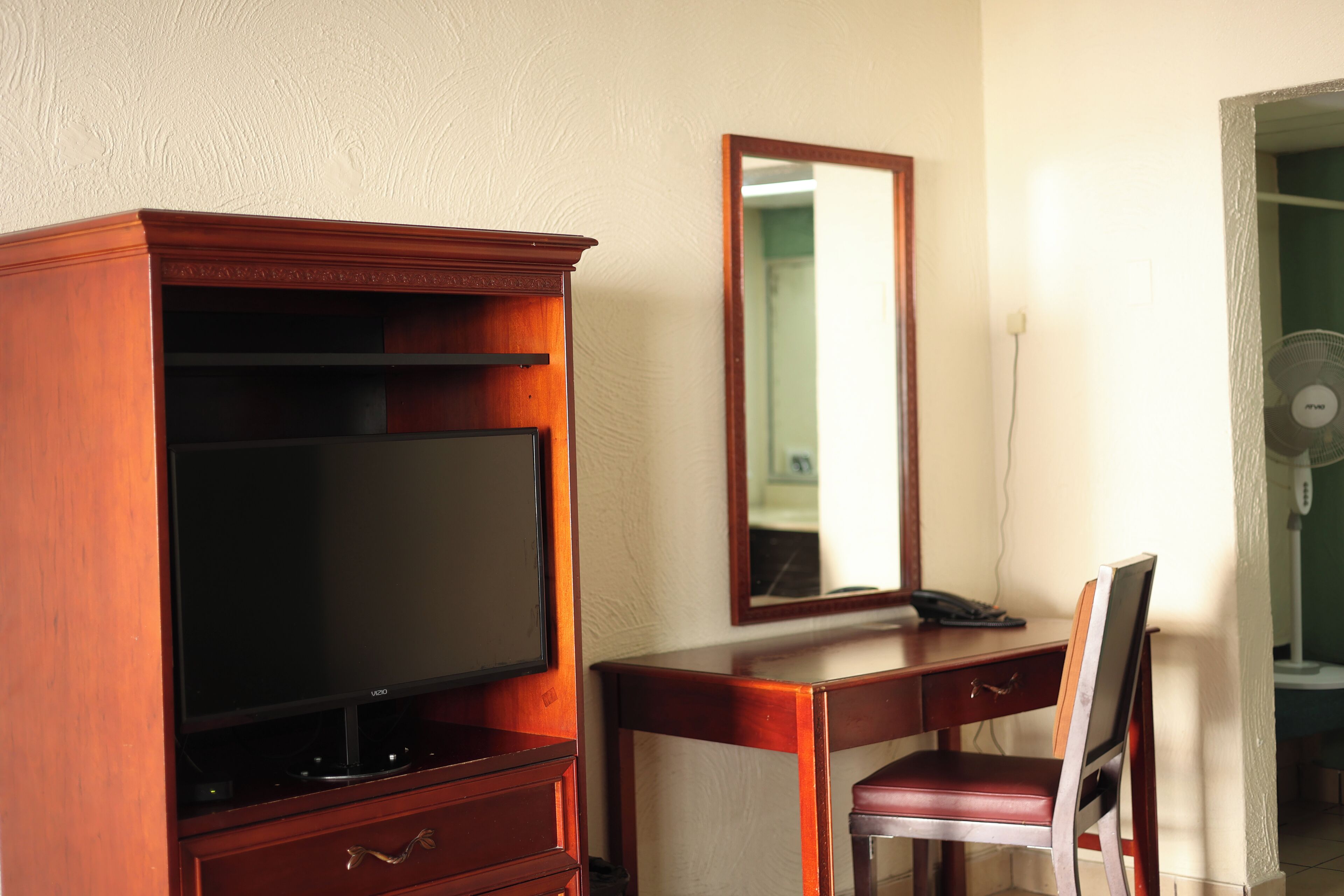 A wooden desk with a television, a chair, and a mirror.