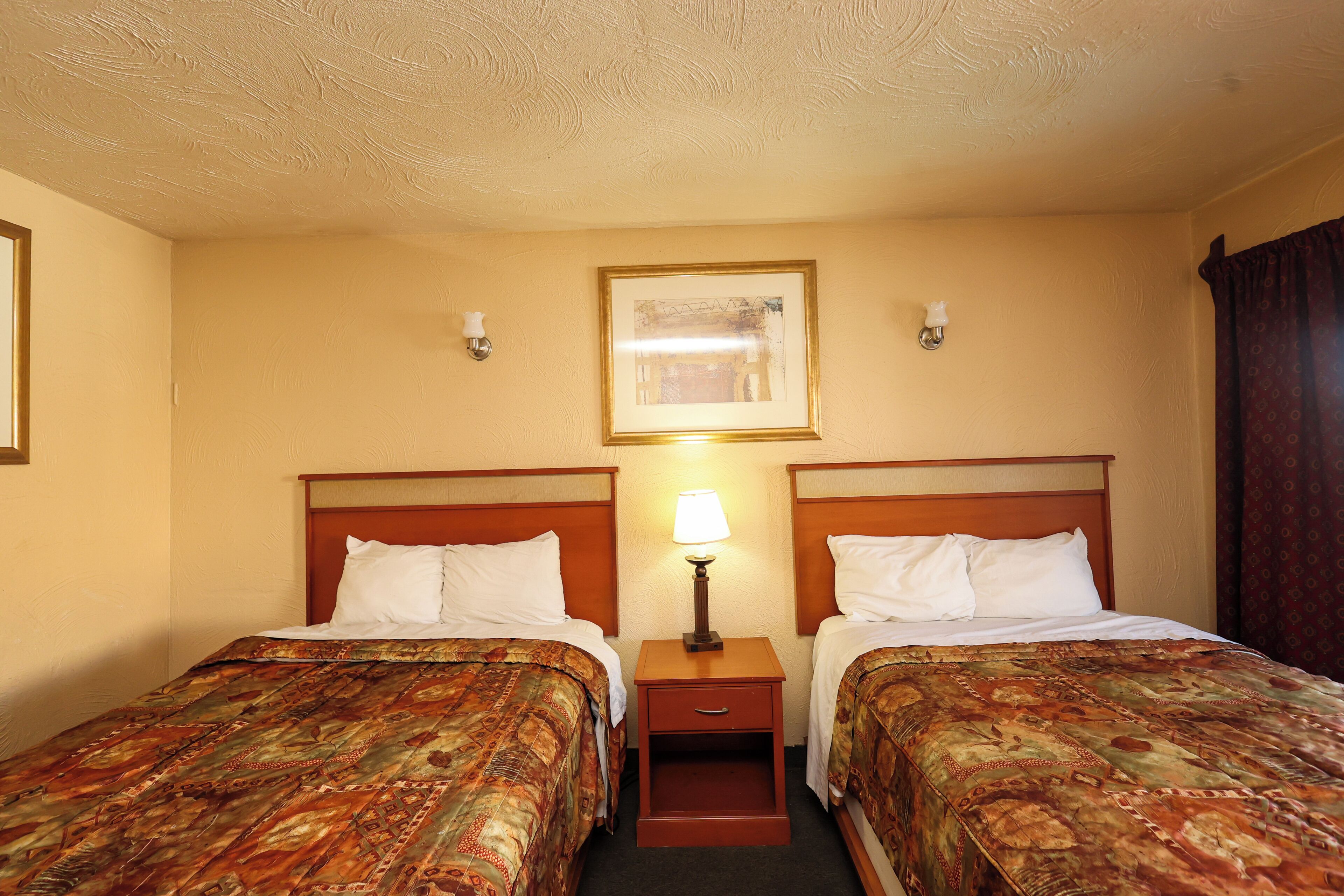 Una camera d'albergo con due letti, un comodino con una lampada e un quadro appeso alla parete.