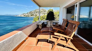 A balcony with a view of the sea and a hillside. There are wooden chairs and a table. - BARCA.Apartment with direct Beach Access (ROSES)