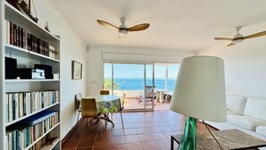 A spacious living room with a large bookshelf, a dining area, and a view of the sea. - BARCA.Apartment with direct Beach Access (ROSES)
