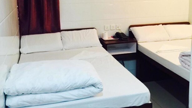 Una camera d'albergo con due letti, un tavolino e un comodino con un telefono e una bottiglia.