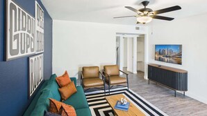 Ein Wohnzimmer mit einer Couch, zwei Sesseln, einem Couchtisch, einem Deckenventilator und einem Fernseher auf einem Schrank.