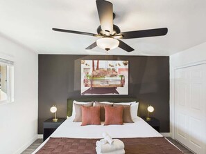 A bedroom with a bed, a ceiling fan, a wall-mounted artwork, bedside lamps, and a door. - Vistas-In Old Town-Walk to Entertainment District (Scottsdale)