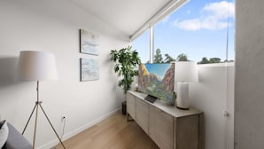 A room with a large window, a desk with a lamp, a painting, and a potted plant. - Lux Beach Retreat: Parking/Wifi (San Diego)