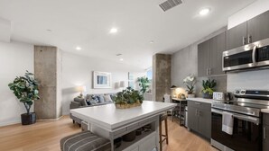 A modern kitchen with a central island, stainless steel appliances, and a dining area with a sofa and plants. - Lux Beach Retreat: Parking/Wifi (San Diego)
