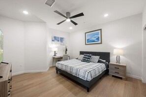 Ein Schlafzimmer mit einem Bett, Nachttischen, einem Deckenventilator und Kunstwerken an der Wand.