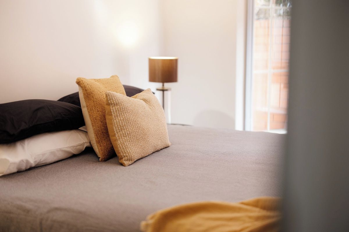 A bed with a grey mattress, two pillows, and a blanket.