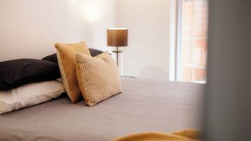 A bed with a grey mattress, two pillows, and a blanket.