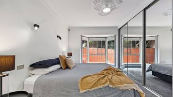 Une chambre à coucher moderne avec un grand lit, une table de chevet, une lampe et une vue sur l’extérieur grâce à une porte vitrée.