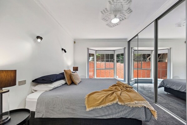 A modern bedroom with a large bed, a bedside table, a lamp, and a view through a glass door.