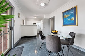 A dining area with a glass table and chairs, a bowl of fruit, and a framed artwork on the wall.