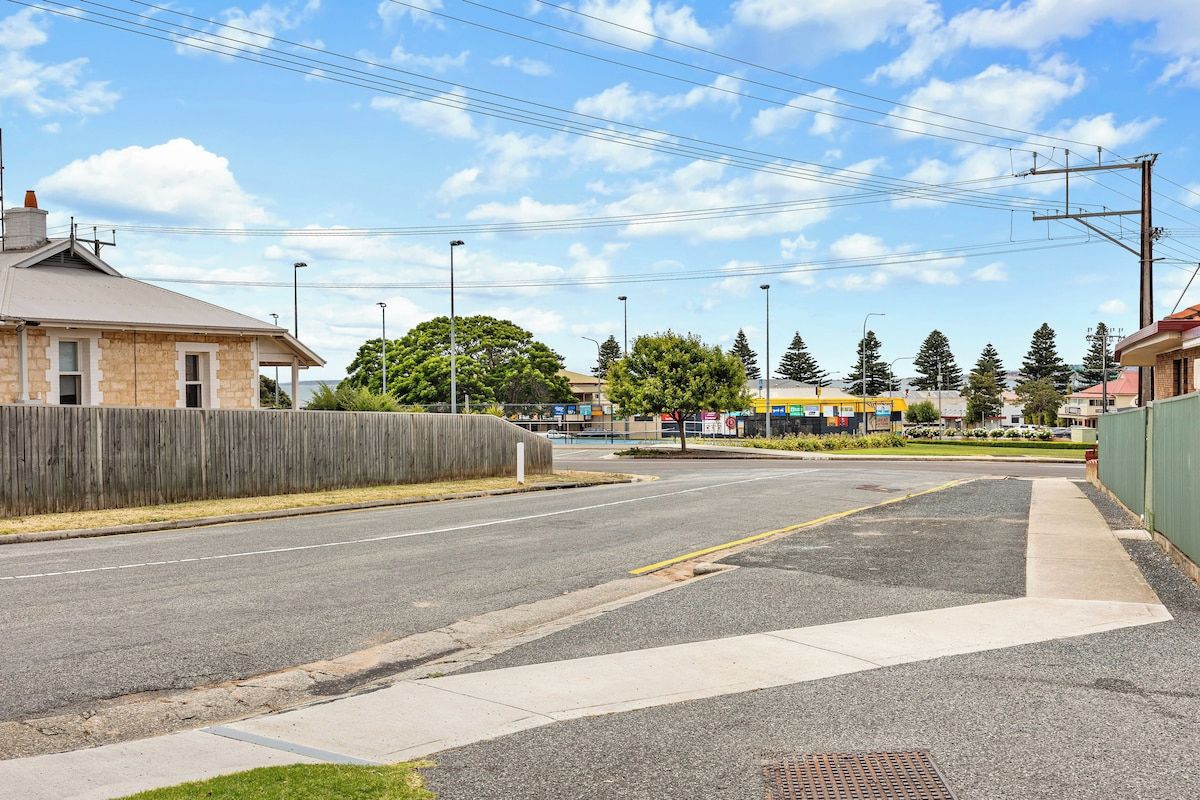 A street view with a building on the left, a sidewalk, and a grassy area.