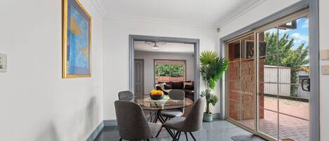 A dining area with a glass table and chairs, a potted plant, and a view through a glass door.