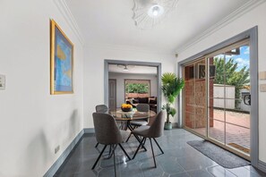 A dining area with a glass table and chairs, a potted plant, and a view through a glass door.