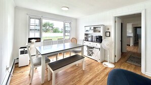 Una cocina con mesa, sillas, banco, ventilador y vistas al exterior.