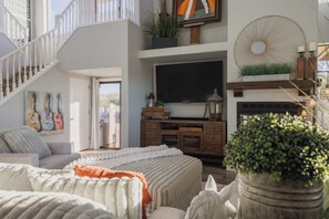 Ein geräumiger Wohnbereich mit Treppe, einem Flachbildfernseher, einem Kamin und einer großen Kübelpflanze.