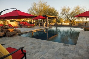 Ein Swimmingpool mit roten Sonnenschirmen, Liegestühlen und einer Pergola.
