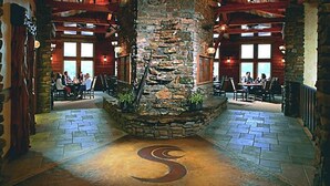 Un restaurant aux murs de pierre, avec un pilier central en pierre et un motif en spirale sur le sol. Les tables et les chaises sont disposées pour accueillir les clients.