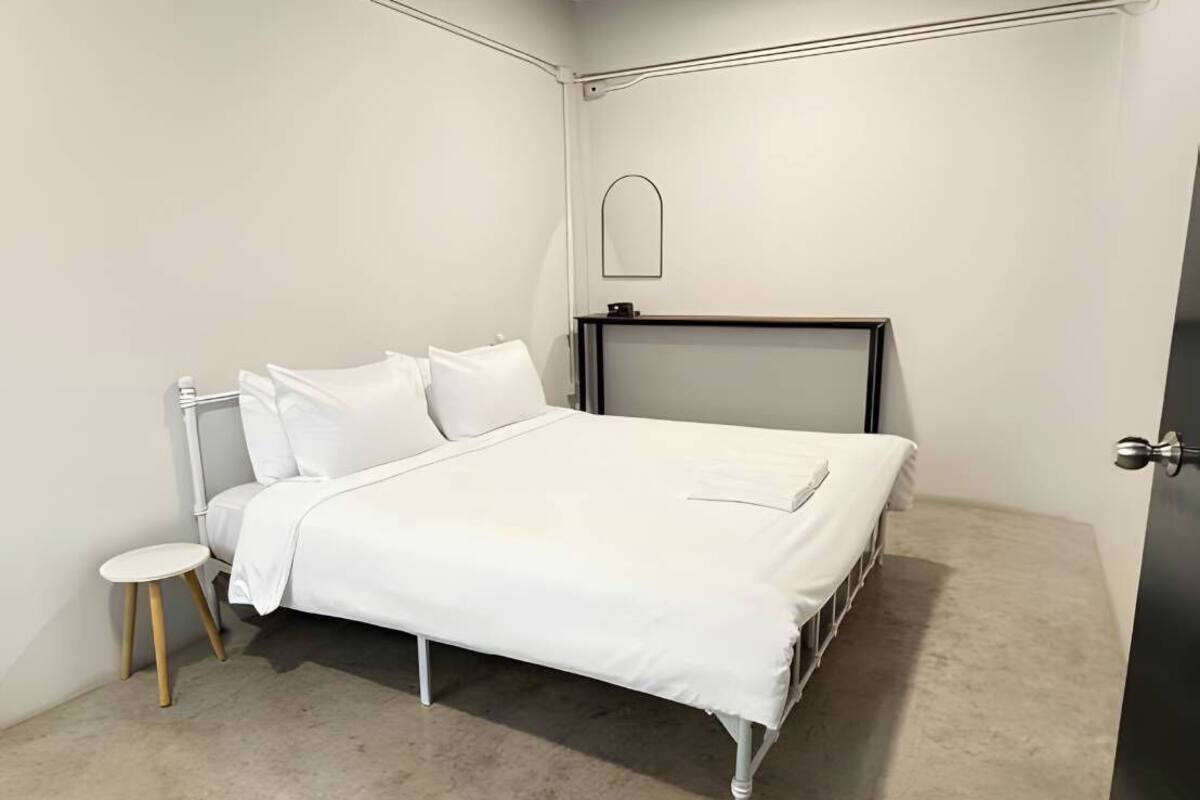 A bedroom with a white bed, a small round table, and a dark-colored door.