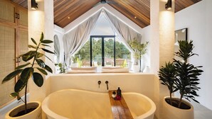 A modern bathroom with a freestanding bathtub, wooden ceiling, and large windows offering a view of greenery. - Villa Joann (Uluwatu)