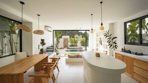A modern kitchen with a central island, wooden dining table, and pendant lighting. - Villa Joann (Uluwatu)