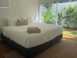 A bedroom with a large bed, a dark-colored headboard, and a view of a garden through a large window. - Spacious Bilinga Beach Stay | Sleeps 6 + Sauna, Unit 5 (Bilinga)