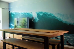 A room with a large wall mural of a surfer riding a wave, a wooden table, and a bench. - Spacious Bilinga Beach Stay | Sleeps 6 + Sauna, Unit 5 (Bilinga)