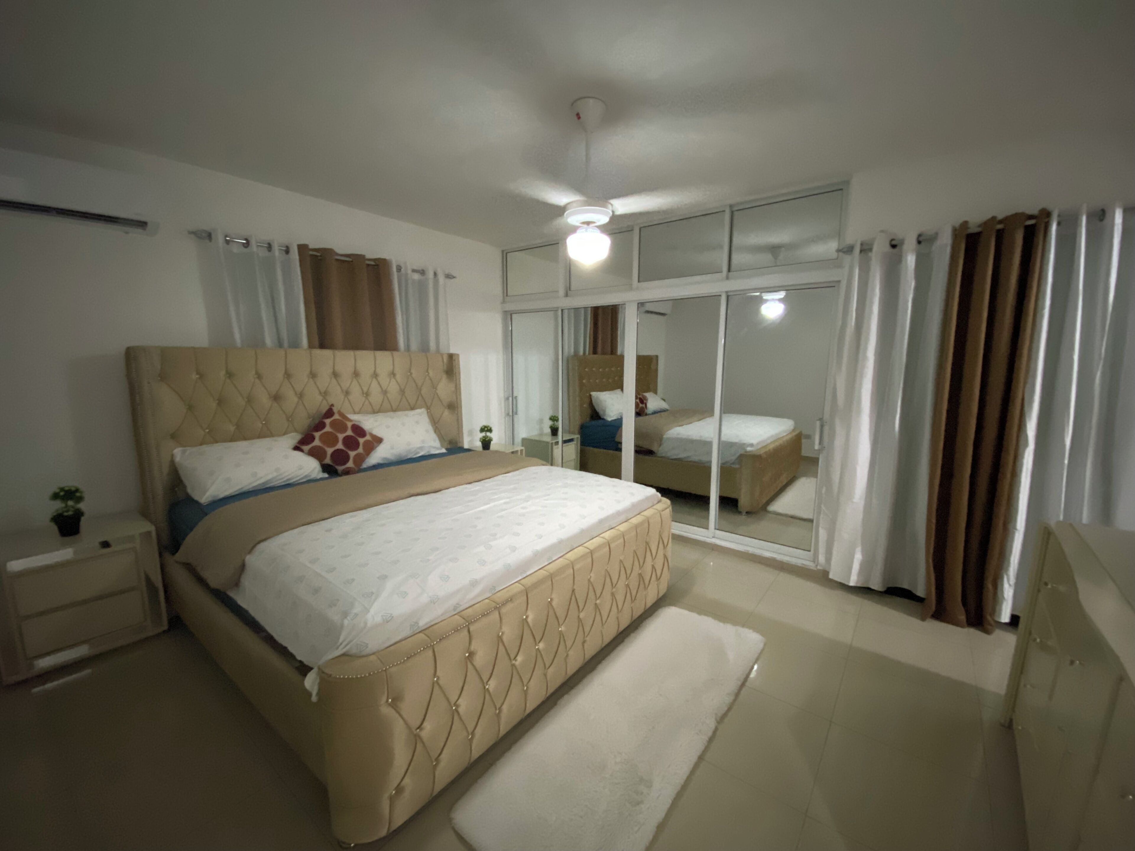 Um quarto com uma cama grande, uma mesinha de cabeceira, um espelho e uma porta de vidro deslizante.