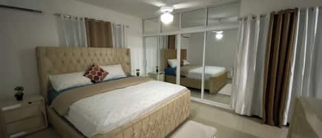 A bedroom with a large bed, a nightstand, a bedside table, a mirror, and a sliding glass door.