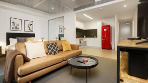 A modern living room with a leather sofa, a coffee table, and a kitchen area with a red refrigerator. - Spacious Studio in a Prime Braddon Location (Braddon)