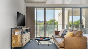 A modern living room with a sofa, a coffee table, and a TV on a wooden cabinet. - Spacious Studio in a Prime Braddon Location (Braddon)