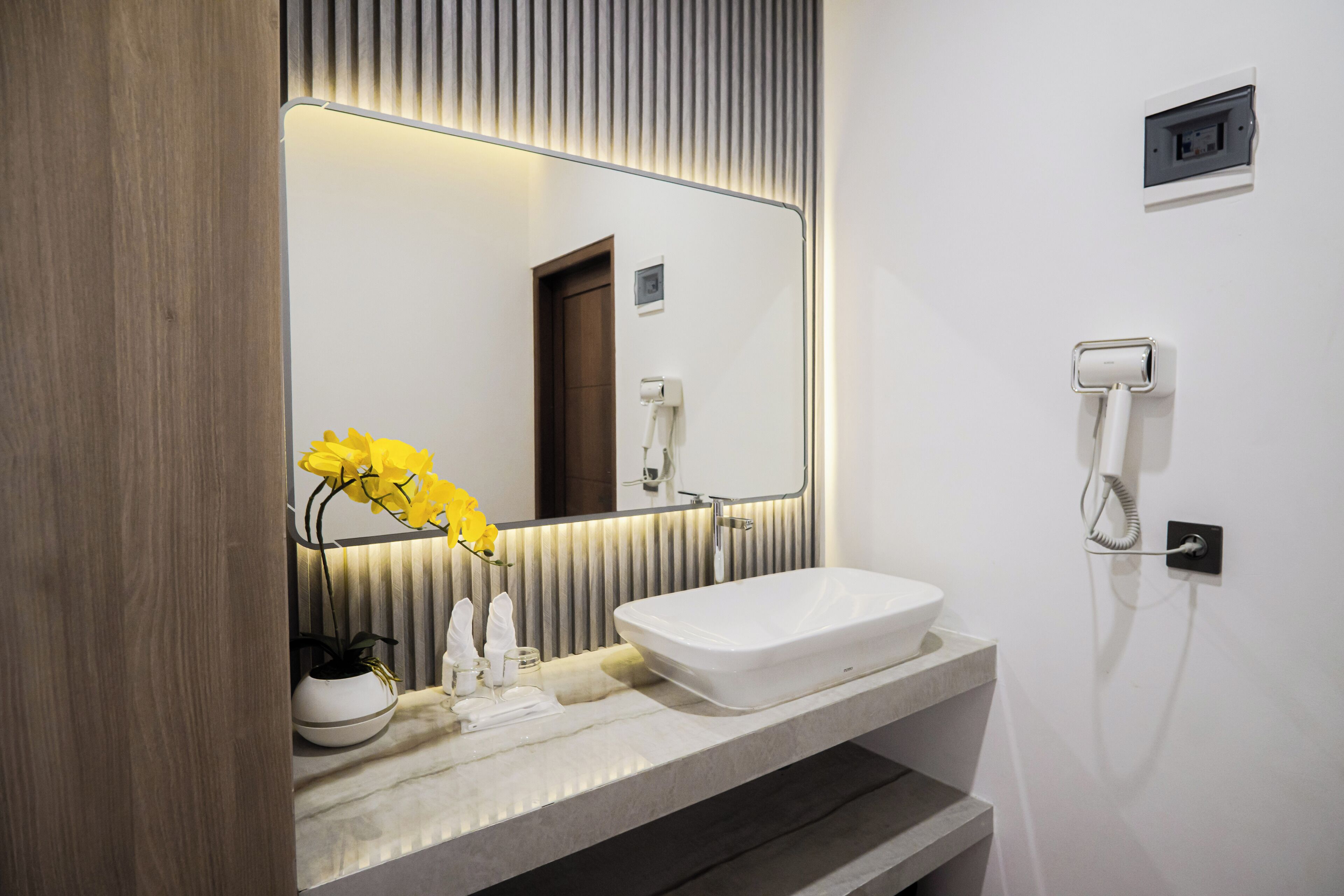 A modern bathroom with a large mirror, a white sink, a towel rack, and a hairdryer on the wall.
