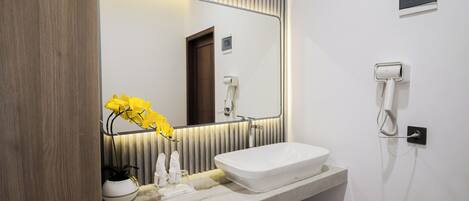 A modern bathroom with a large mirror, a white sink, a towel rack, and a hairdryer on the wall.