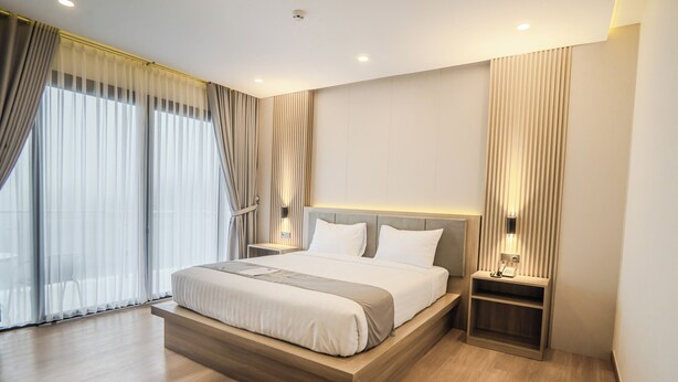 A modern hotel room with a large bed, wooden platform, bedside tables, and a view of the city through floor-to-ceiling windows. - Orion Villa Telaga Menjer (Garung)
