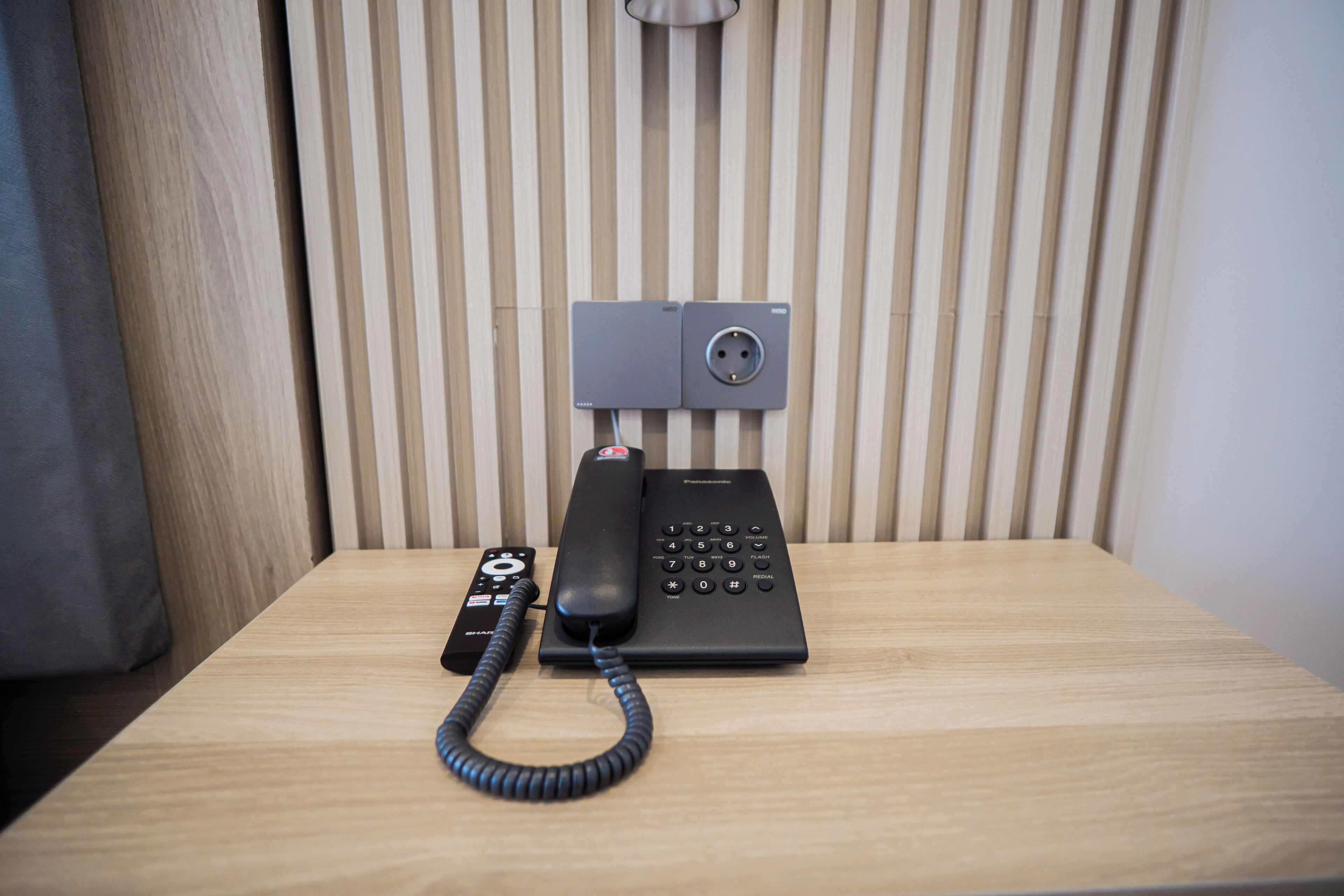 Une chambre d’hôtel avec une table en bois, un téléphone noir et une télécommande.