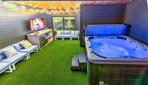 Ein Garten mit Whirlpool, einer Couch, einem Fernseher und einem kleinen Tisch mit Getränken.