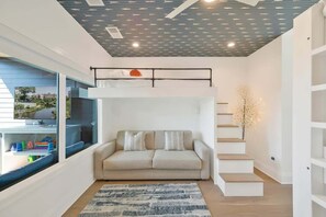 Un salon moderne avec un canapé, un tapis à motifs, un escalier et une vue dégagée sur l’extérieur grâce à une grande fen être.