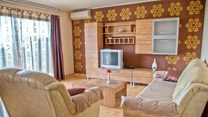 A living room with two beige sofas, a coffee table, a TV, and patterned wallpaper. - Holiday apartment with air conditioning (Maružini)