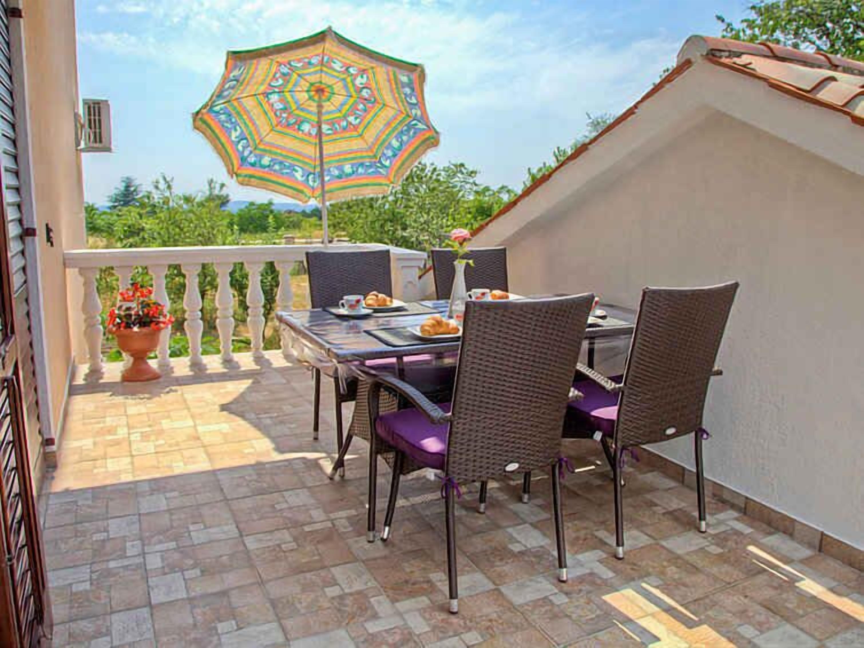 Une terrasse avec une table et des chaises, un parasol décoratif et une plante en pot.
