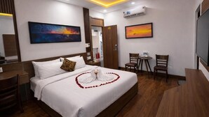 Habitación de hotel con una cama bien hecha, un escritorio, dos sillas y cuadros en las paredes.