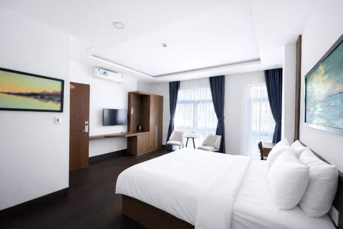 A modern hotel room with a large bed, a desk, a TV, and a seating area.