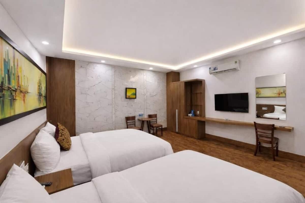A hotel room with two beds, a desk, a TV, and a painting on the wall.