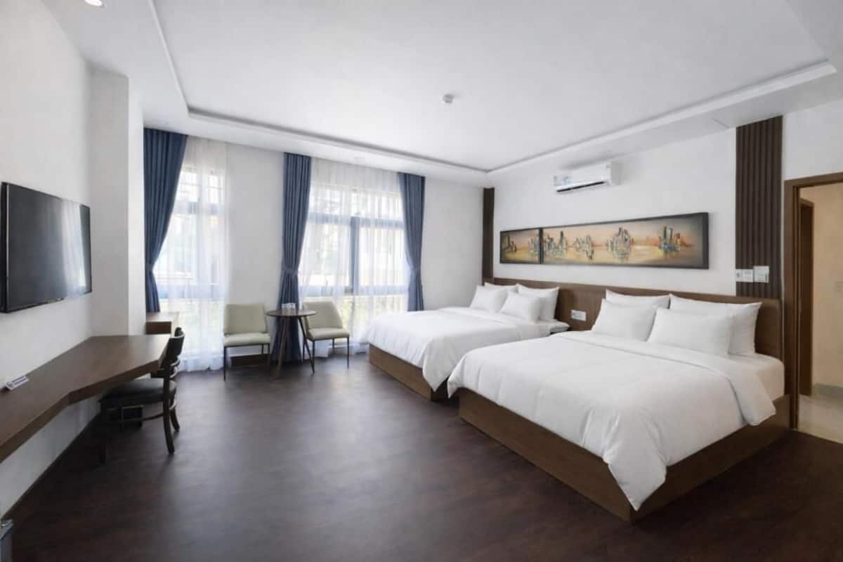 A hotel room with two beds, a desk, a chair, a TV, and a painting on the wall.