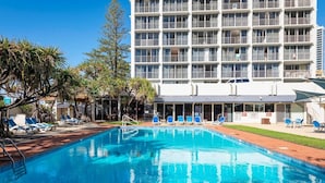 Un hôtel doté d’une piscine, de chaises longues et d’un bâtiment comportant de nombreux balcons.