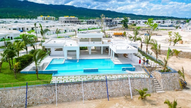 Un complexe hôtelier moderne doté d’une piscine centrale, entourée de palmiers et d’un mur de pierre.