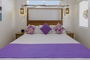 A bed with a purple bedspread, white linens, and floral pillows. There are two bedside tables with lamps, a window with curtains, and a wall clock. - 320 - One Bedroom Ocean View, Vivo Resorts (Bajos de Chila)