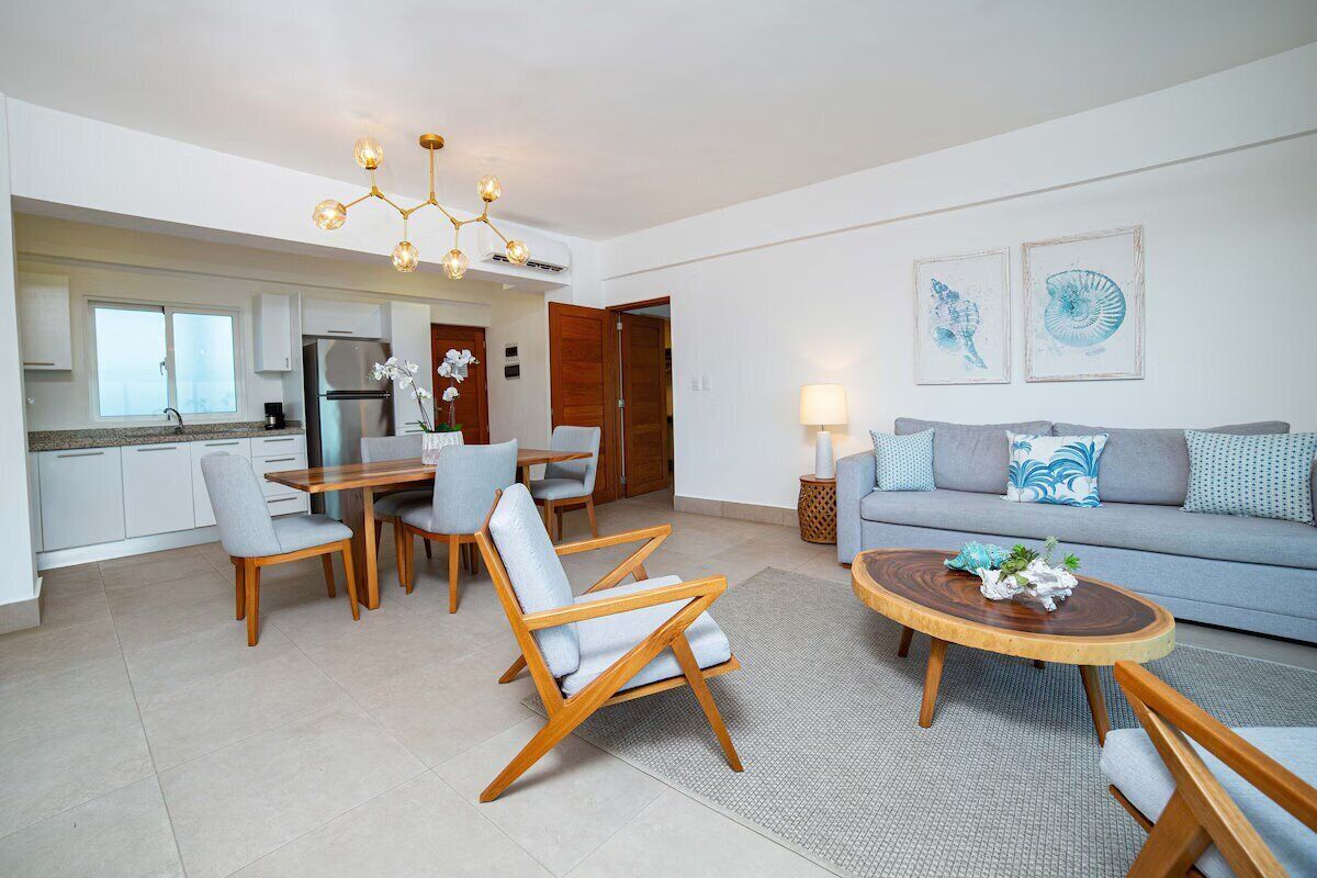 Ein modernes Wohnzimmer mit Sofa, Couchtisch und Sesseln. Es gibt einen Essbereich mit Tisch und Stühlen. Der Raum verfügt über eine Chandelier und Kunstwerke an der Wand.