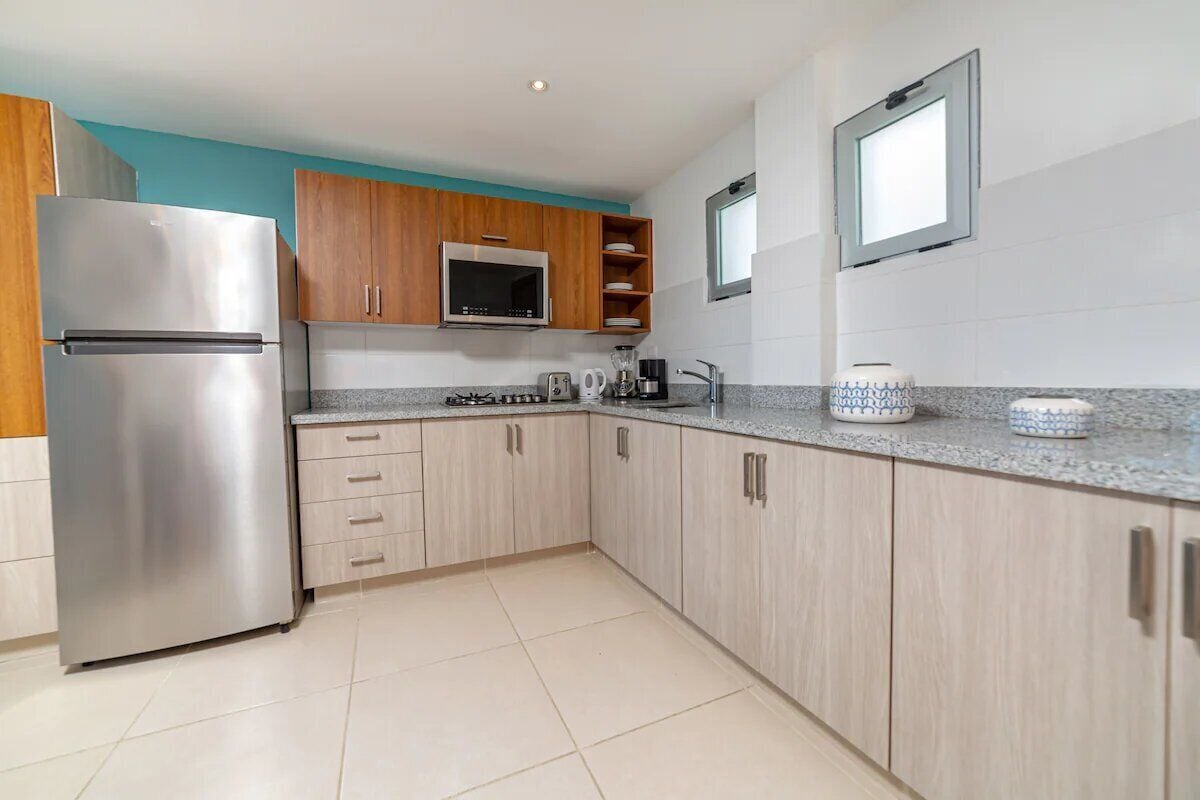 A modern kitchen with light wood cabinets, stainless steel appliances, and a granite countertop.